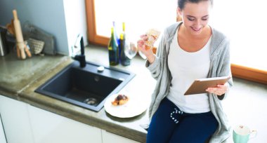 Mutfakta dijital tablet kullanan güzel genç bir kadın.