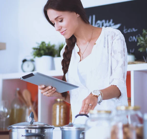 Mutfakta yemek yapmak için tablet bilgisayar kullanan genç bir kadın.