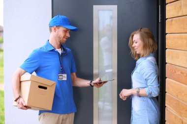 Mavi üniformalı gülümseyen kurye servis konseptine paket kutusu teslim eden teslimatçı.