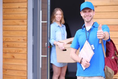 Mavi üniformalı gülümseyen kurye servis konseptine paket kutusu teslim eden teslimatçı.