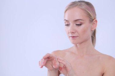 Mutlu gülümseyen genç bir kadının portresi tenine dokunuyor ya da krem sürüyor, beyaz arka planda izole edilmiş.