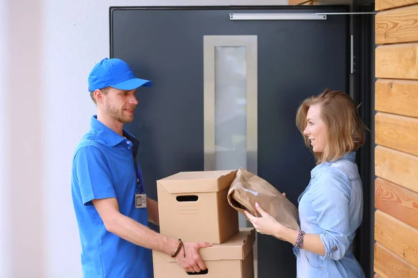 Leende leverans man i blå uniform leverera paket låda till mottagaren - kurir service koncept — Stockfoto