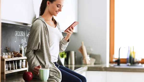 Vrouw met behulp van mobiele telefoon zitten in moderne keuken — Stockfoto