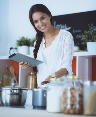 Mutfakta yemek yapmak için tablet bilgisayar kullanan genç bir kadın.