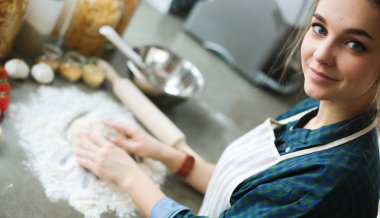 Güzel bir kadın mutfakta pasta pişiriyor. Masanın yanında duruyor.