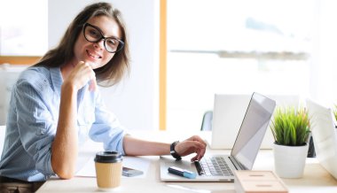 Ofis masasında dizüstü bilgisayarıyla oturan genç bir kadın.