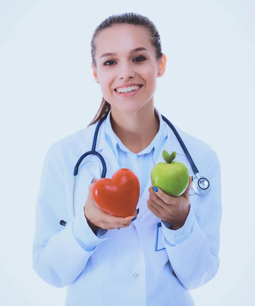 Beautiful smiling female doctor holding red heart and green apple — Stock Photo, Image