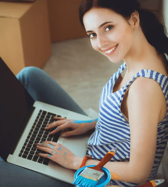 Retrato de mujer joven mientras pinta nuevo apartamento, sentado con el ordenador portátil — Foto de Stock