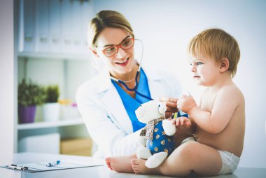 Kadın doktor, klinikte steteskoplu bir çocuğu dinliyor.