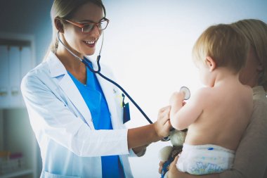 Kadın doktor, klinikte steteskoplu bir çocuğu dinliyor.