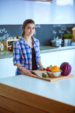 Masanın yanındaki mutfakta sebze doğrayan genç bir kadın..