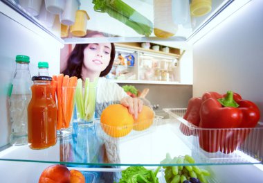 Sağlıklı yiyecek, sebze ve meyvelerle dolu açık buzdolabının yanında duran kadın portresi. Kadın portresi