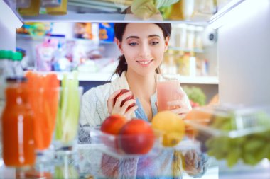 Sağlıklı yiyecek, sebze ve meyvelerle dolu açık buzdolabının yanında duran kadın portresi. Kadın portresi