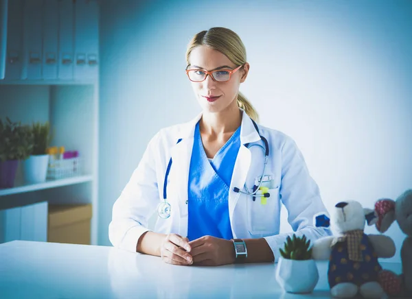 Mooie jonge glimlachende vrouwelijke arts zittend aan het bureau. — Stockfoto