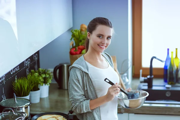 Mujer joven prepara panqueques en la cocina mientras está de pie cerca de la mesa. Mujer en la cocina. Cocinar en la cocina. —  Fotos de Stock