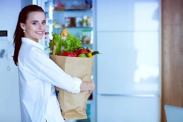 Young woman holding grocery shopping bag with vegetables .Standing in the kitchen. Woman in the kitchen looking at the camera — Stock Photo, Image