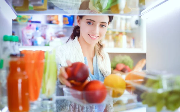 Retrato de una mujer parada cerca de una nevera abierta llena de alimentos saludables, verduras y frutas. Retrato de mujer —  Fotos de Stock