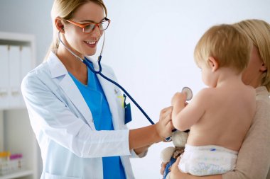 Kadın doktor, klinikte steteskoplu bir çocuğu dinliyor.