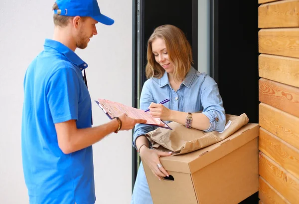 Repartidor sonriente con uniforme azul que entrega la caja de paquetes al destinatario: concepto de servicio de mensajería. Repartidor sonriente en uniforme azul — Foto de Stock