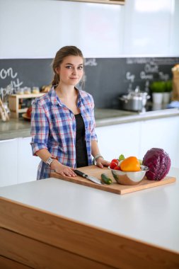 Masanın yanındaki mutfakta sebze doğrayan genç bir kadın..