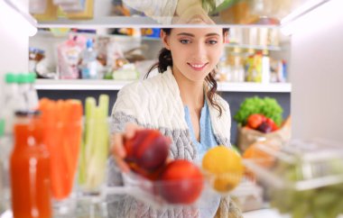 Sağlıklı yiyecek, sebze ve meyvelerle dolu açık buzdolabının yanında duran kadın portresi. Kadın portresi