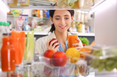 Sağlıklı yiyecek, sebze ve meyvelerle dolu açık buzdolabının yanında duran kadın portresi. Kadın portresi