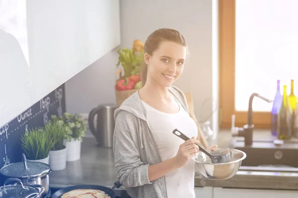 Mujer joven prepara panqueques en la cocina mientras está de pie cerca de la mesa. Mujer en la cocina. Cocinar en la cocina. —  Fotos de Stock