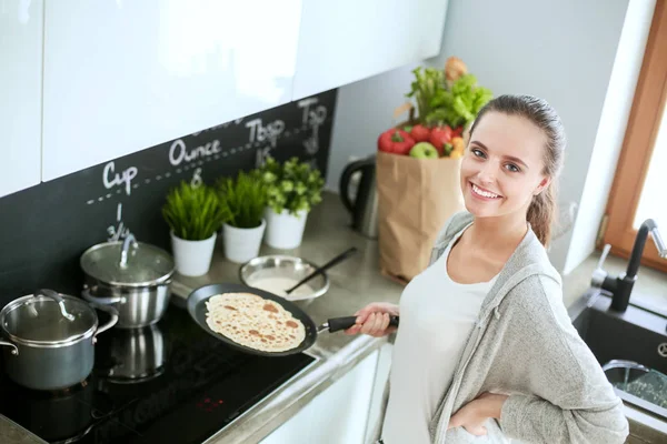 Mujer joven prepara panqueques en la cocina mientras está de pie cerca de la mesa. Mujer en la cocina. Cocinar en la cocina. —  Fotos de Stock