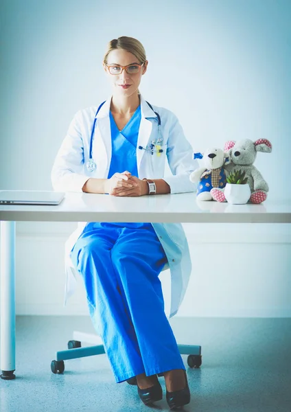 Mooie jonge glimlachende vrouwelijke arts zittend aan het bureau. — Stockfoto