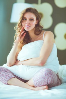 Yatağında otururken bir yastık tutan genç kadın.