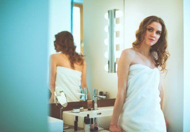 Genç bir kadın aynaya bakıyor ve makyaj yapıyor..