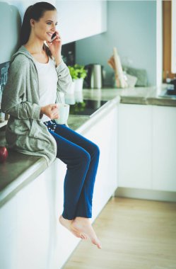 modern mutfakta otururken cep telefonu kullanan kadın.