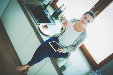 Mutfakta dijital tablet kullanan güzel genç bir kadın..