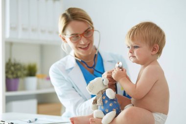Kadın doktor, klinikte steteskoplu bir çocuğu dinliyor.