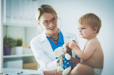 Kadın doktor, klinikte steteskoplu bir çocuğu dinliyor.