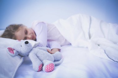 çocuk oyuncak oyuncak ayı ile yatakta uyur küçük kız.