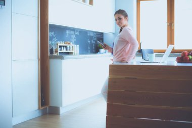 Cep telefonu ayakta modern mutfak kullanan kadın.