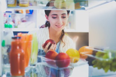 Sağlıklı yiyecek, sebze ve meyvelerle dolu açık buzdolabının yanında duran kadın portresi. Kadın portresi