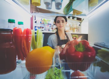 Sağlıklı yiyecek, sebze ve meyvelerle dolu açık buzdolabının yanında duran kadın portresi. Kadın portresi