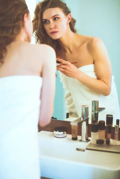 Jonge vrouw kijken in de spiegel en zetten make-up op. — Stockfoto