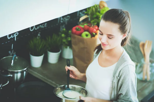 Mujer joven prepara panqueques en la cocina mientras está de pie cerca de la mesa. Mujer en la cocina. Cocinar en la cocina. — Foto de Stock
