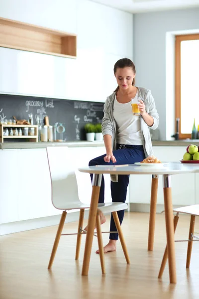 Ung kvinna med apelsinjuice och tablett i köket. — Stockfoto