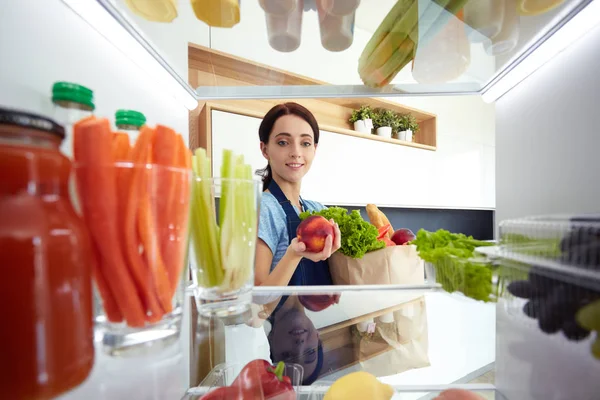 Retrato de una mujer parada cerca de una nevera abierta llena de alimentos saludables, verduras y frutas. Retrato de mujer — Foto de Stock