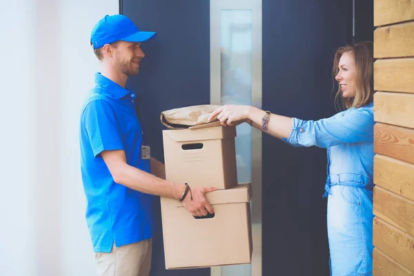 Smiling delivery man in blue uniform delivering parcel box to recipient - courier service concept. Smiling delivery man in blue uniform