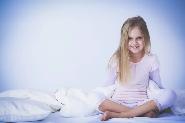 Liten flicka i sovrummet sitter på sängen. Lilla flickan bär en pyjamas och sitter i sängen . — Stockfoto