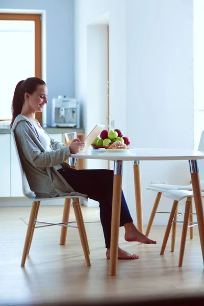 Mujer joven con jugo de naranja y tableta en la cocina. — Foto de Stock