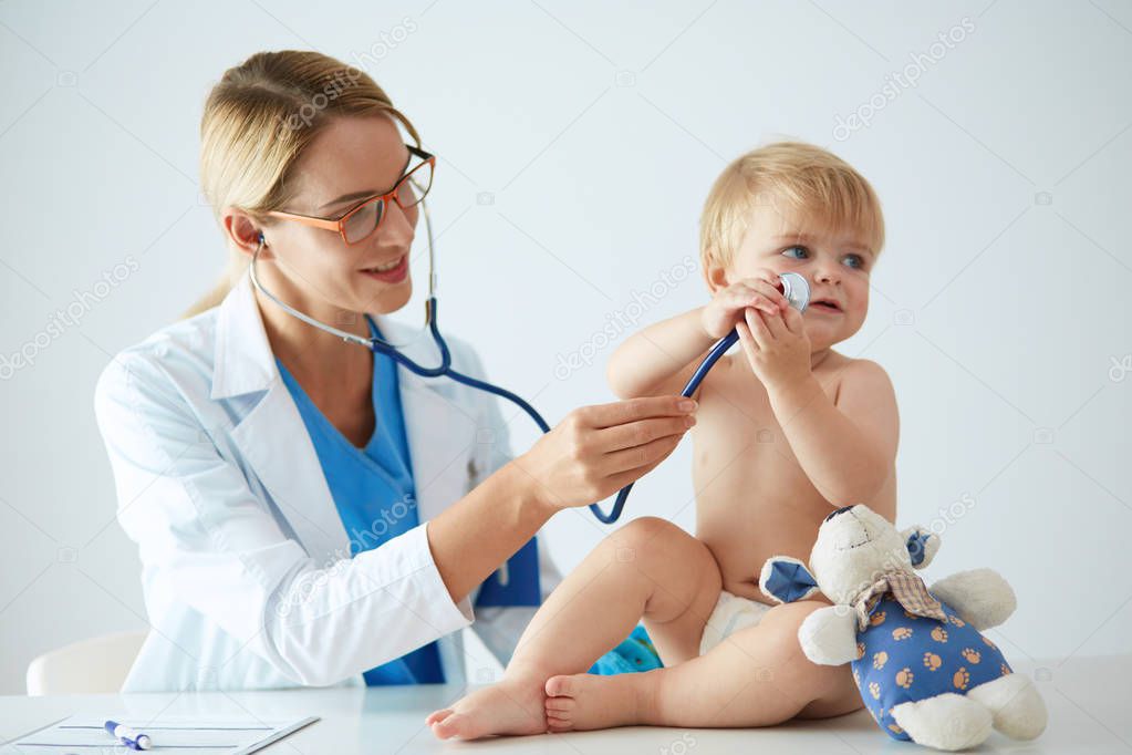 Female doctor is listening kid with a stethoscope in clinic