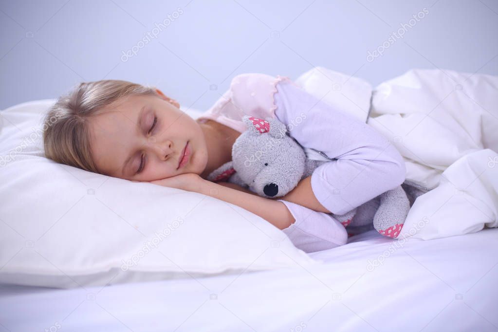 Child little girl sleeps in the bed with a toy teddy bear.