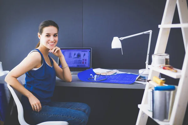 Jonge vrouw zit aan het bureau met instrumenten, plan en laptop — Stockfoto