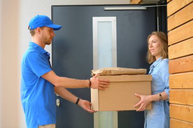 Mavi üniformalı gülümseyen kurye servis konseptine paket kutusu teslim eden teslimatçı. Mavi üniformalı gülümseyen teslimatçı.